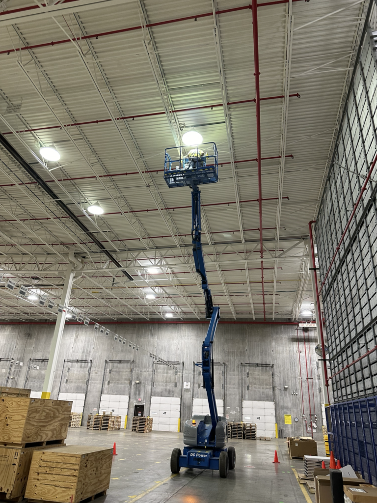 High-bay lighting installation in warehouse ceiling using boom lift by Del Haven Electric